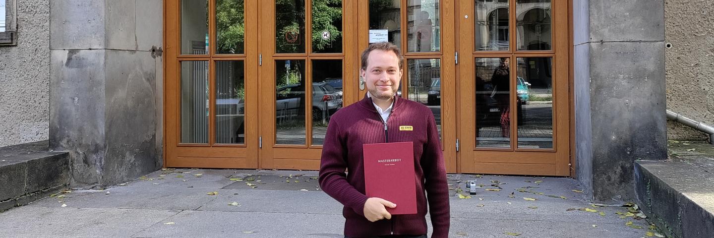 Kristof Halasz hält seine Masterarbeit in der Hand