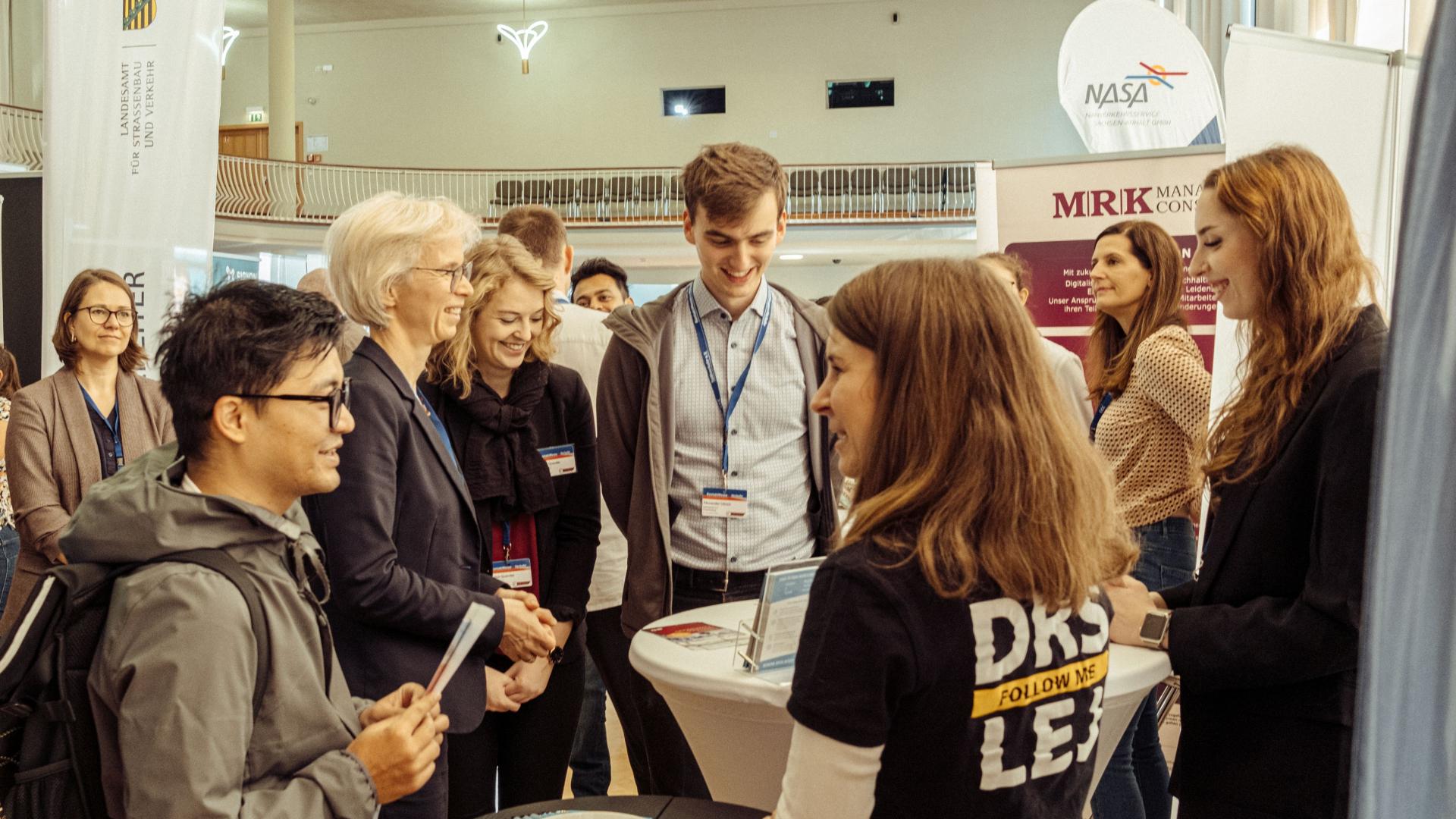 Eine Gruppe von Menschen unterhält sich an einem Messestand