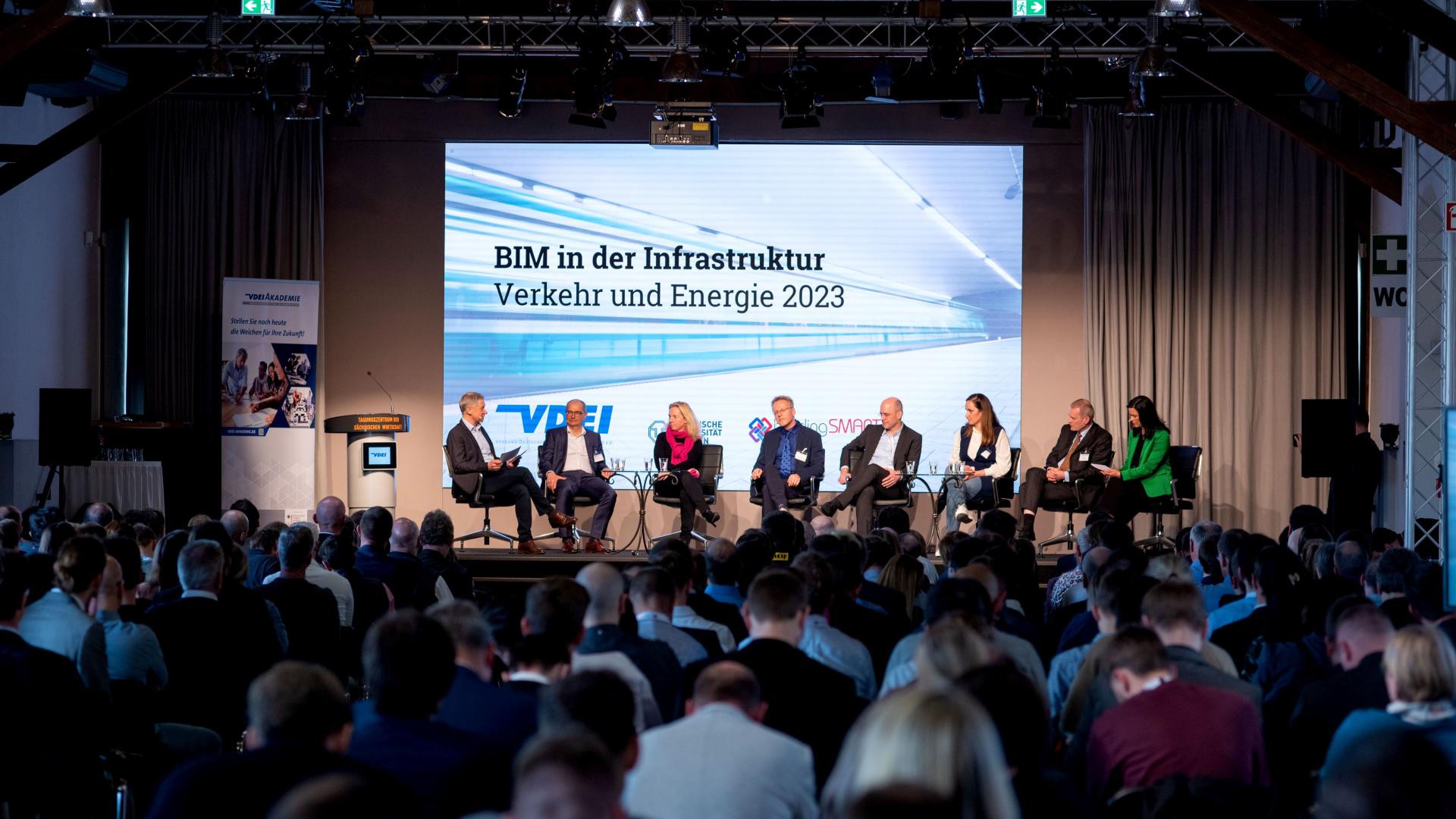 Ein Podiumsgespräch auf einer Bühne mit 8 Teilnehmenden vor vielen Zuschauern