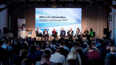 Ein Podiumsgespräch auf einer Bühne mit 8 Teilnehmenden vor vielen Zuschauern