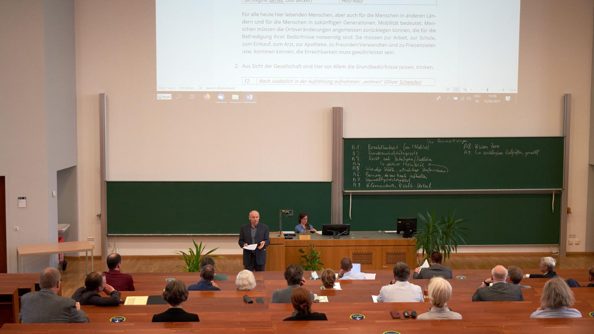 A lecture hall with people sitting at intervals.