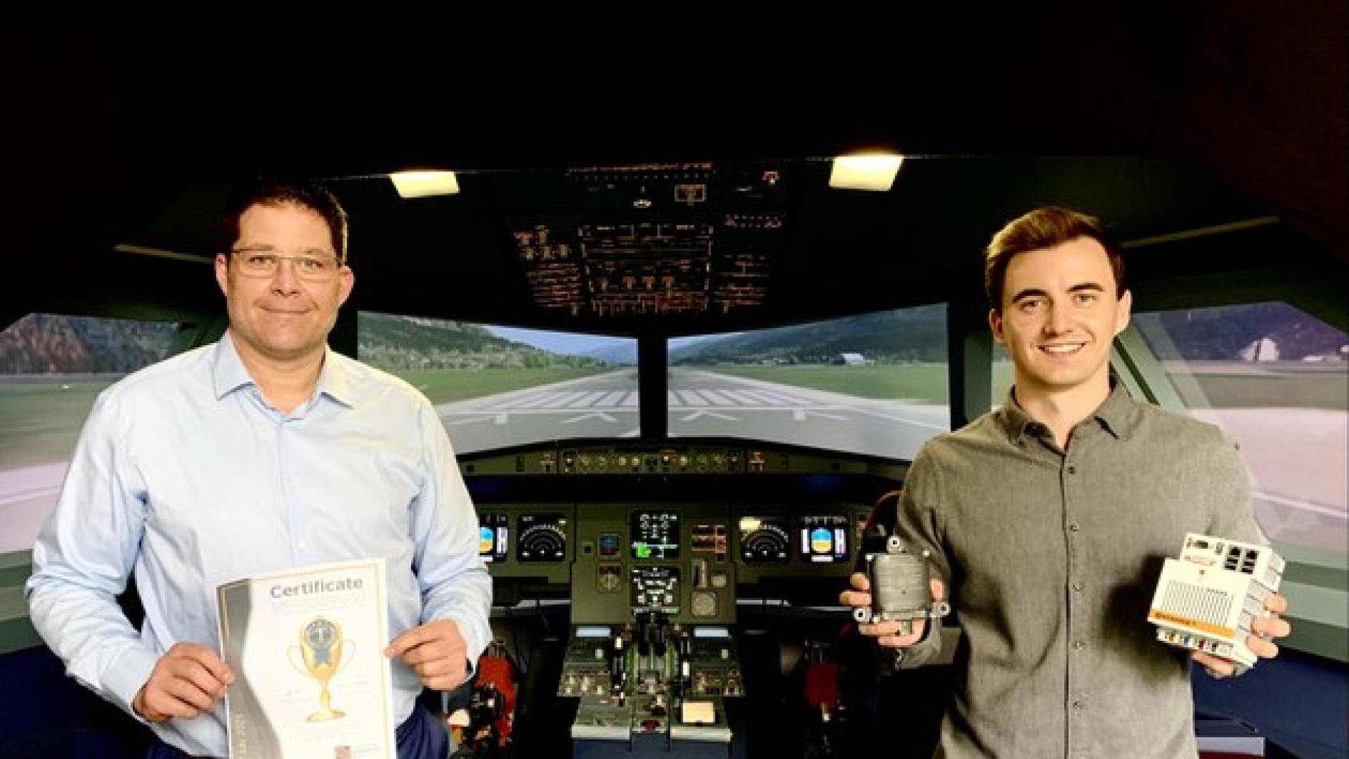  Two men stand in an aircraft cockpit. One of them holds a certificate in his hands.
