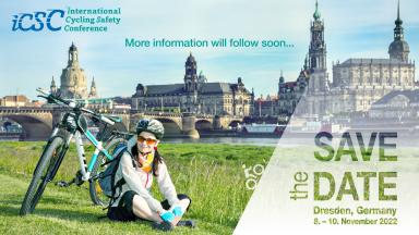 A cyclist sits on a meadow, her bike next to her, the old town of Dresden in the background.