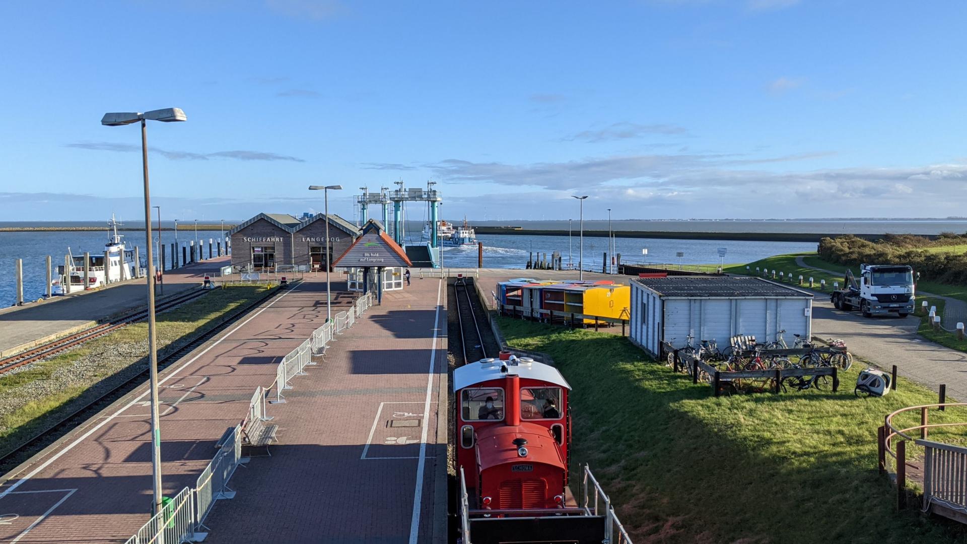 In the foreground is a railway, in the back a station and the North Sea