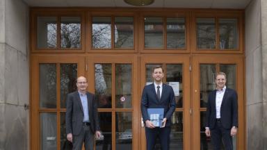Drei Männer stehen vor der großen Holzeingangstür der Fakultät Verkehrswissenschaften.