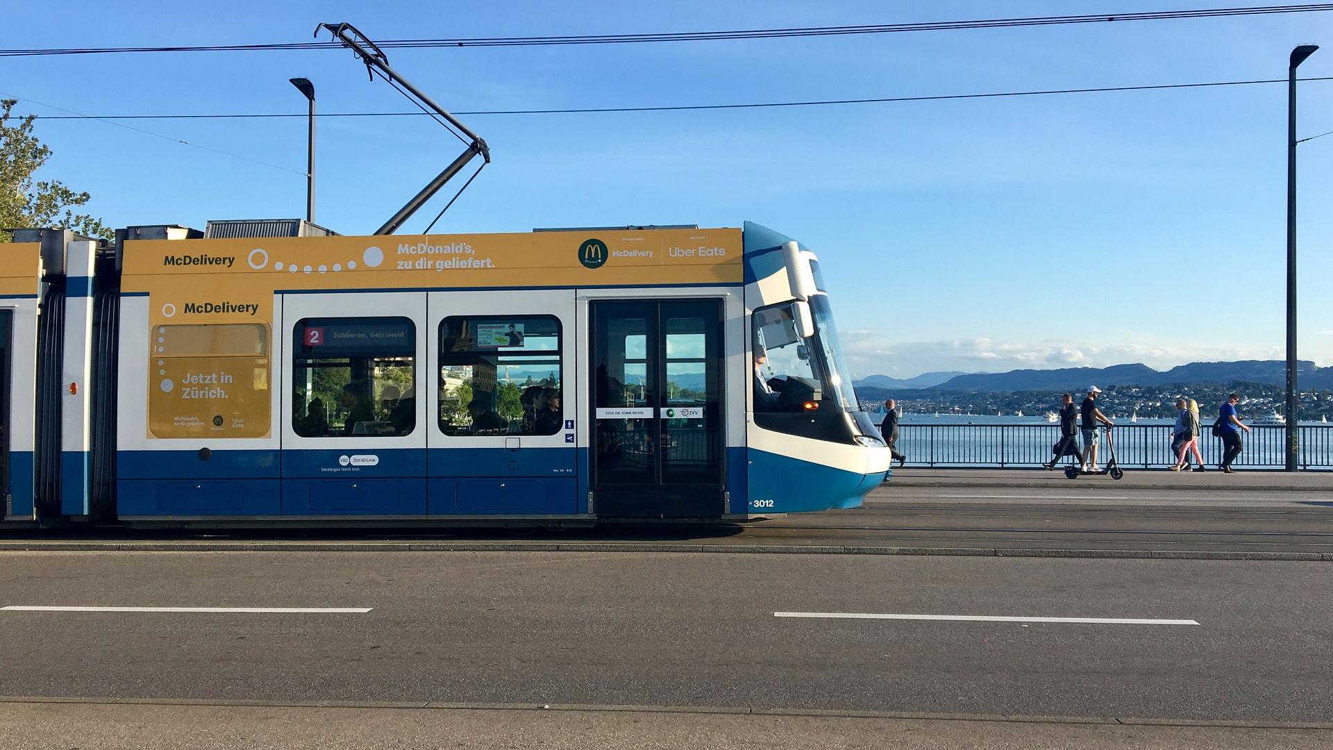 A blue and white tram is crossing a bridge in Zurich.