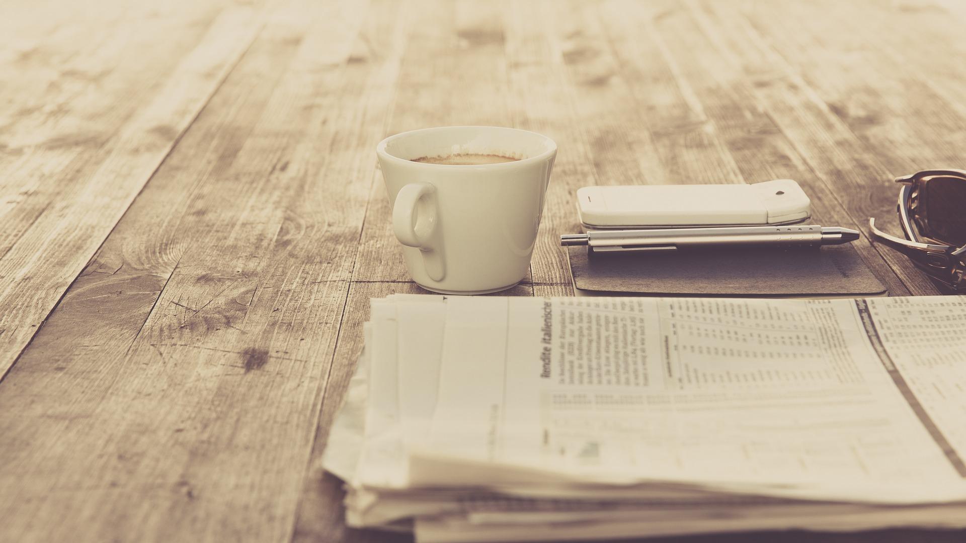 a newspaper lies on the table, next to it a cup of coffee.