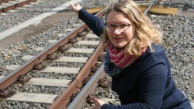 Eine Frau mit blonden Haaren und Brille hockt an einer Bahnschiene und zeigt auf etwas.