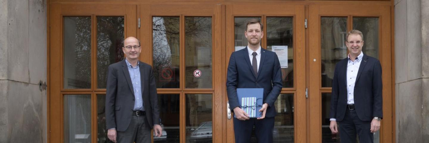 Drei Männer stehen vor der großen Holzeingangstür der Fakultät Verkehrswissenschaften.