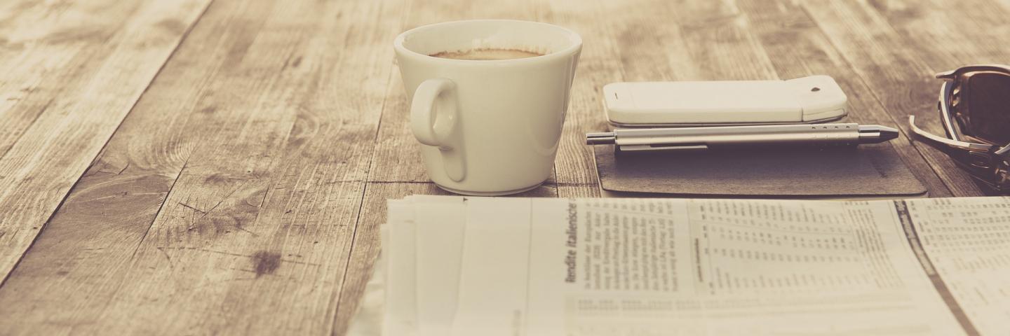 a newspaper lies on the table, next to it a cup of coffee.