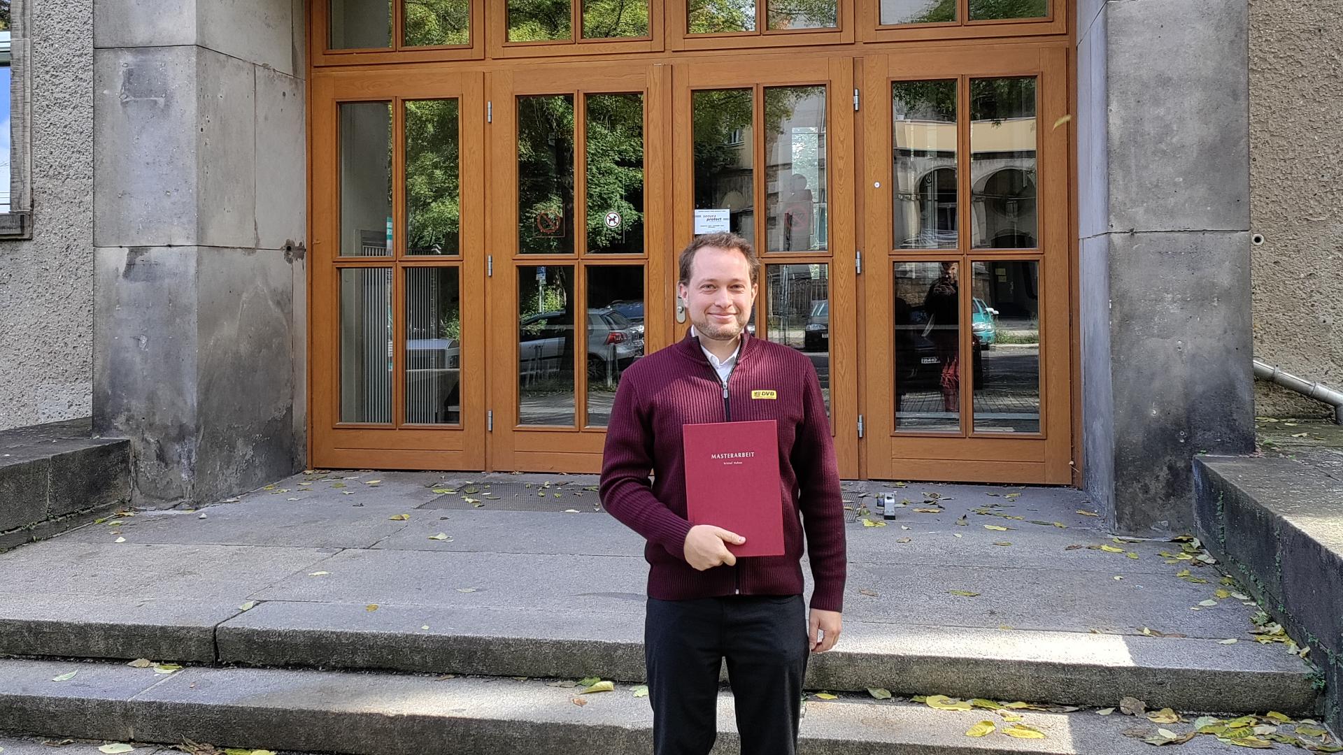 Kristof Halasz hält seine Masterarbeit in der Hand